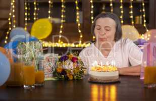 Elderly woman blowing candles at her birthday celebration