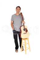 Man standing with his guitar holding it on a chair