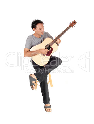 Young casual man playing the guitar and sitting