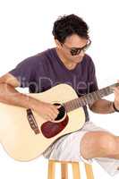 Young casual dressed man playing the guitar and sitting