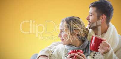 Composite image of  cheerful couple in winter clothing holding cups against window