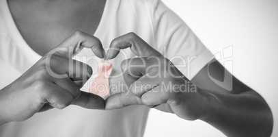 Women making heart with their fingers around pink ribbon