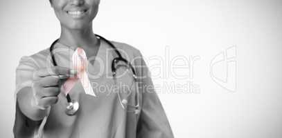Smiling nurse holding breast cancer awareness pink ribbon between her fingers