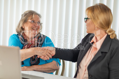 Senoir Woman Shaking Hands with Businesswoman Near Laptop Comput