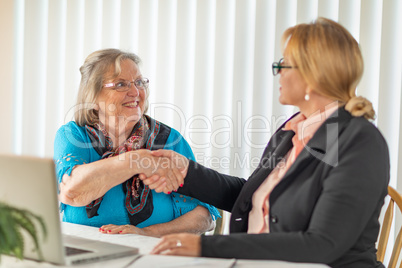 Senoir Woman Shaking Hands with Businesswoman Near Laptop Comput