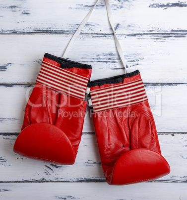 pair of leather worn red boxing gloves hanging on a white lace