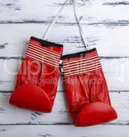pair of leather worn red boxing gloves hanging on a white lace