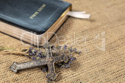 Christian cross on lavanda flowers next to Holy Bible