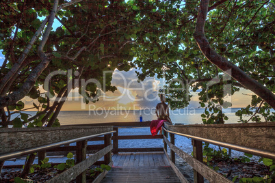 Young woman sits on a fence overlooking the ocean and beach in B