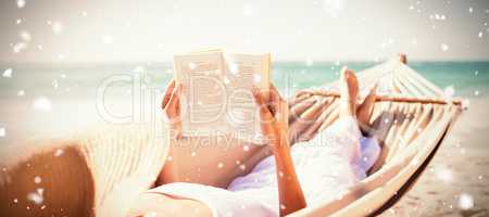Composite image of woman reading book on hammock at beach