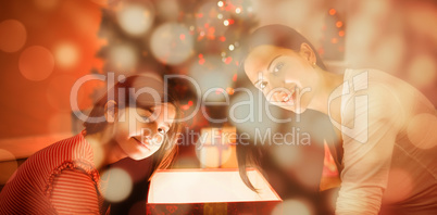 Composite image of festive mother and daughter opening a glowing christmas gift