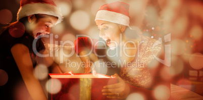 Composite image of festive mother and daughter opening a glowing christmas gift