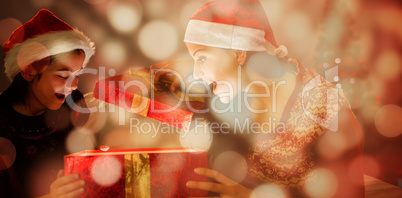 Composite image of festive mother and daughter opening a glowing christmas gift