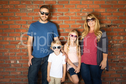 Young Caucasian Family Wearing Sunglasses Against Brick Wall