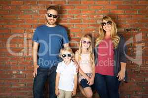 Young Caucasian Family Wearing Sunglasses Against Brick Wall