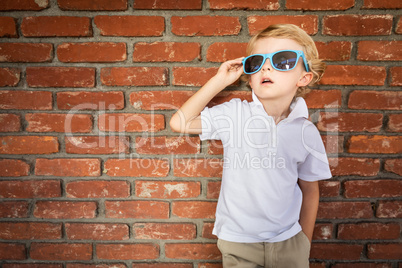 Cute Young Caucasian Boy Wearing Sunglasses Against Brick Wall