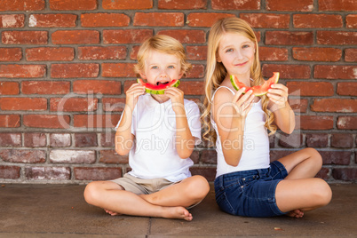 Cute Young Cuacasian Boy and Girl Eating Watermelon Against Brick wall