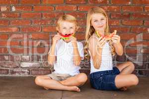 Cute Young Cuacasian Boy and Girl Eating Watermelon Against Brick wall