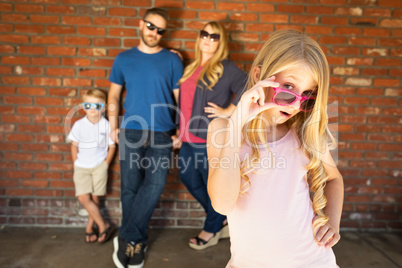 Cute Young Caucasian Girl Wearing Sunglasses with Family Behind