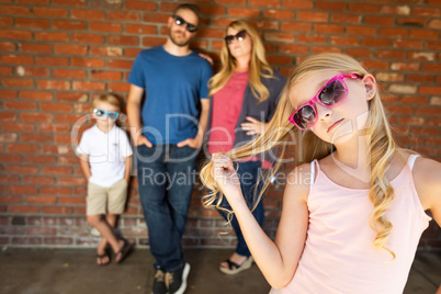 Cute Young Caucasian Girl Wearing Sunglasses with Family Behind