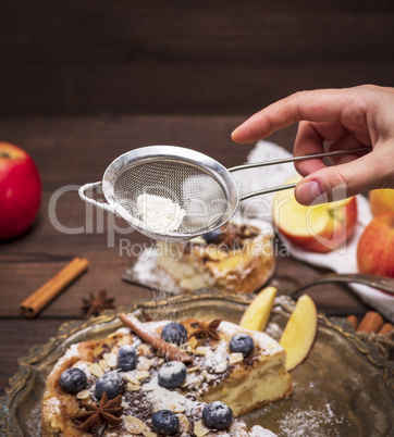 female hand holding a kitchen strainer over apple pie