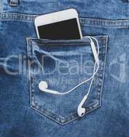 smartphone with headphones in the back pocket of blue jeans