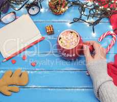 woman's hand holding a red ceramic mug with hot chocolate and ma