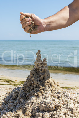 hand builds a castle from the wet sea sand