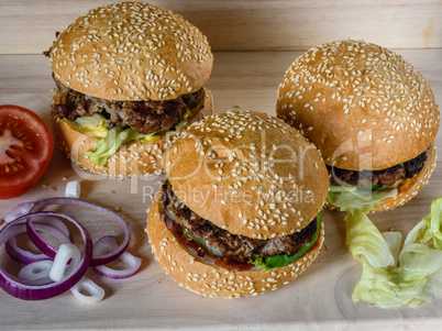 Three fresh burger lay on the board with vegetables