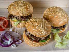 Three fresh burger lay on the board with vegetables