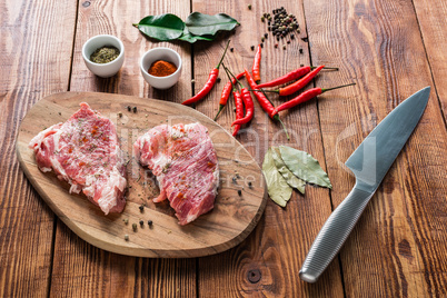 Raw steaks with spices and knife on wooden table.