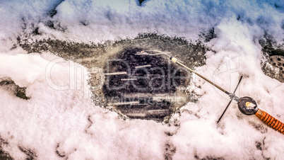 A fishing rod lies near the hole in the ice on the river in winter. Winter fishing in the snowfall.