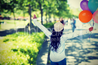 Composite image of full length rear view of carefree woman holding colorful balloons