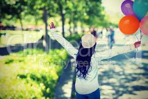 Composite image of full length rear view of carefree woman holding colorful balloons