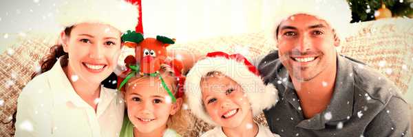 Composite image of portrait of a happy family with christmas hats sitting on the sofa