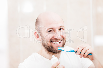 Smiling bald man holding toothbrush with toothpaste and brushing teeth