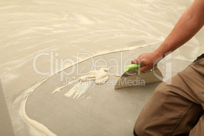 Work on laying flooring. Worker installing new vinyl tile floor.