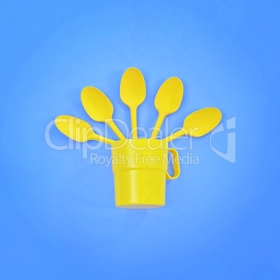 A yellow plastic mug and spoons lay in it on a bright blue background. The concept of a holiday, a picnic.