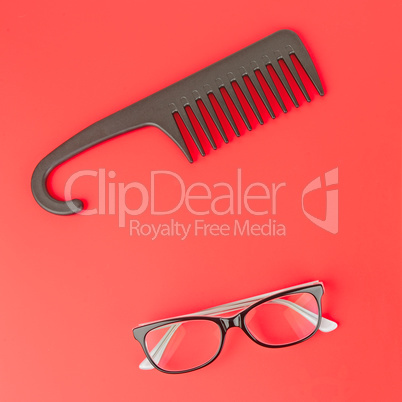 Stylish glasses and hairbrush on a red background.