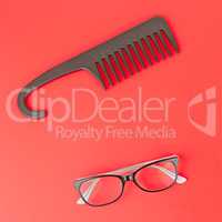 Stylish glasses and hairbrush on a red background.