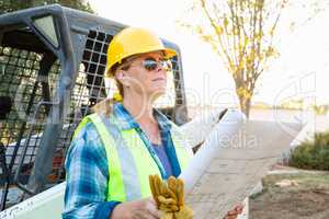 Female Worker Holding Technical Blueprints Near Small Bulldozer