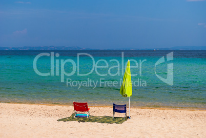Morning on the sandy beach on the Greek coast. Lonely umbrella and two chairs vacationers