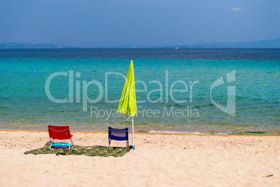 Morning on the sandy beach on the Greek coast. Lonely umbrella and two chairs vacationers