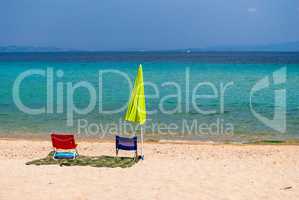 Morning on the sandy beach on the Greek coast. Lonely umbrella and two chairs vacationers
