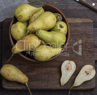 ripe green pears in a brown clay bowl on a table