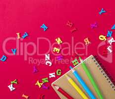 notebook and multicolored wooden pencils on a red background