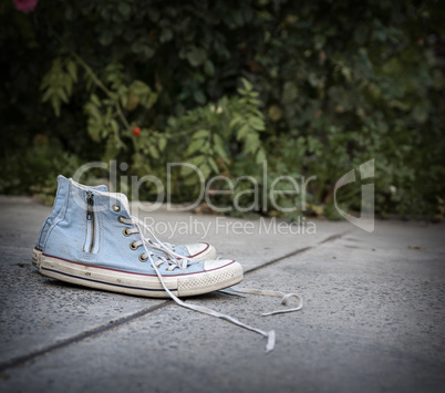 pair of old worn blue textile sneakers on gray asphalt