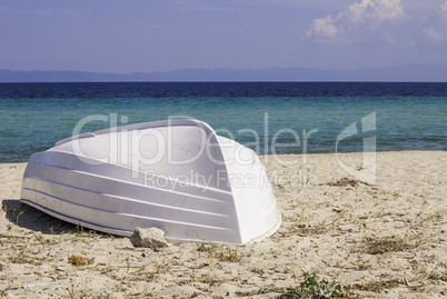 Old white fishing boat, lying on a sandy beach on the shore of the Aegean sea in Greece