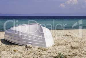 Old white fishing boat, lying on a sandy beach on the shore of the Aegean sea in Greece