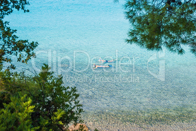 Sea view through pine forest. Tourists swim with a mask in the sea. Halkidiki Greece